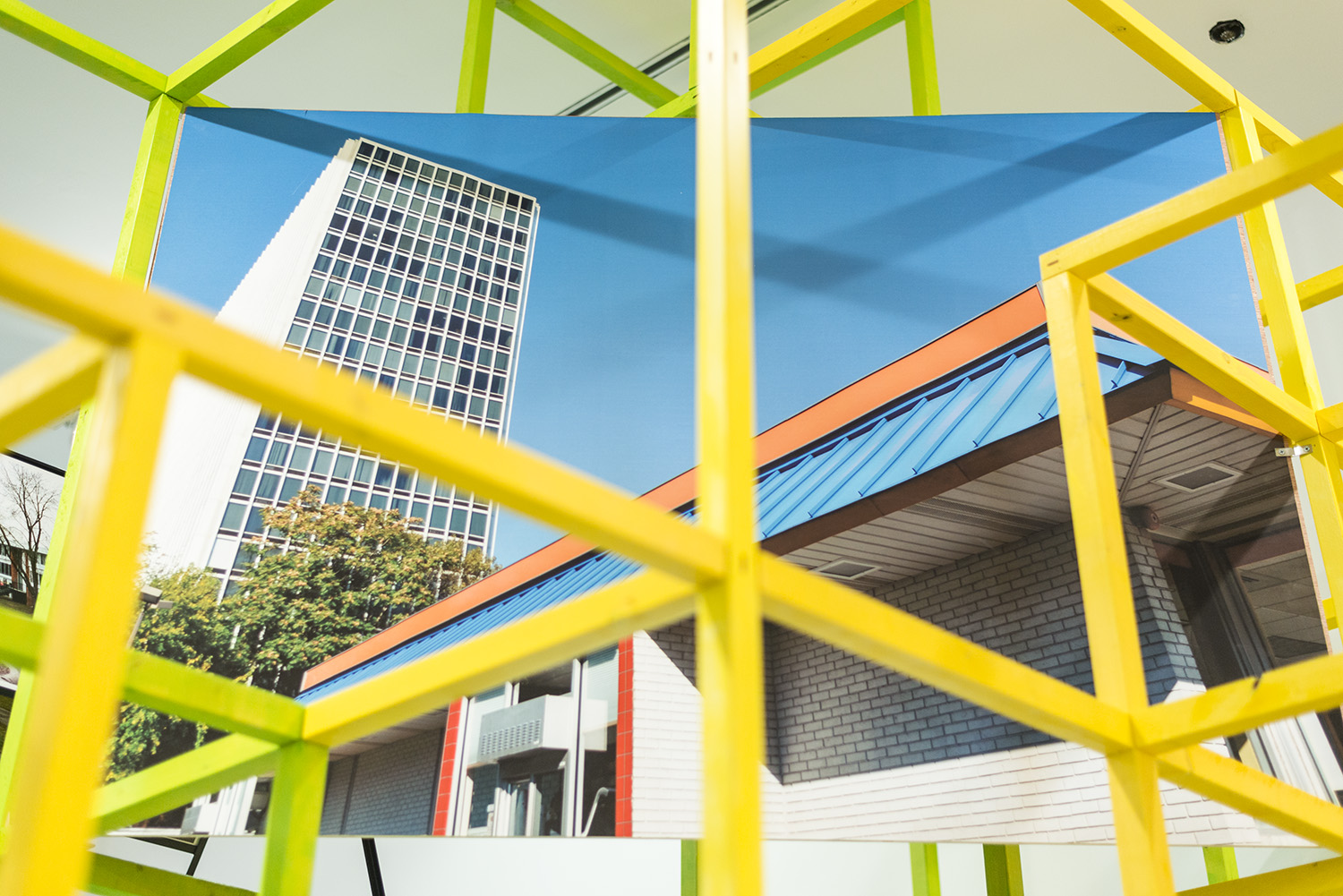yellow metal grid over a photo of a tall white building against a blue sky