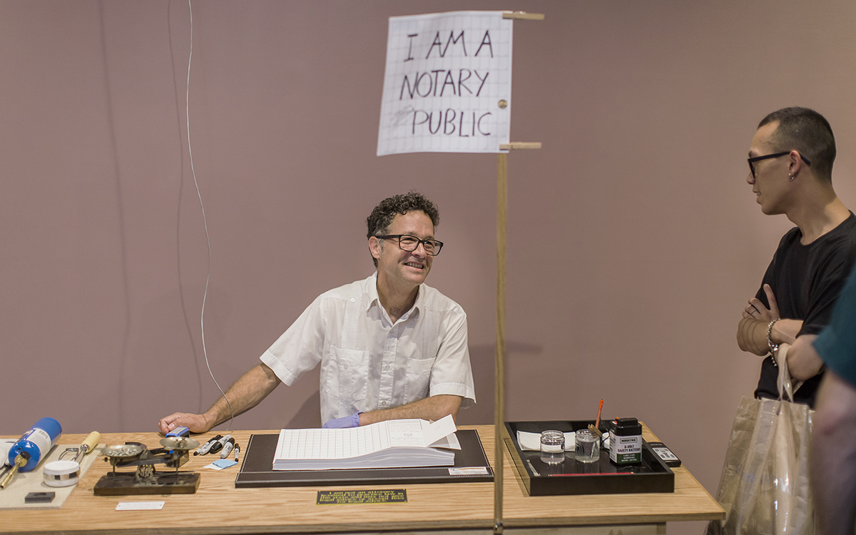 a man at a table with a sign and table visitors 