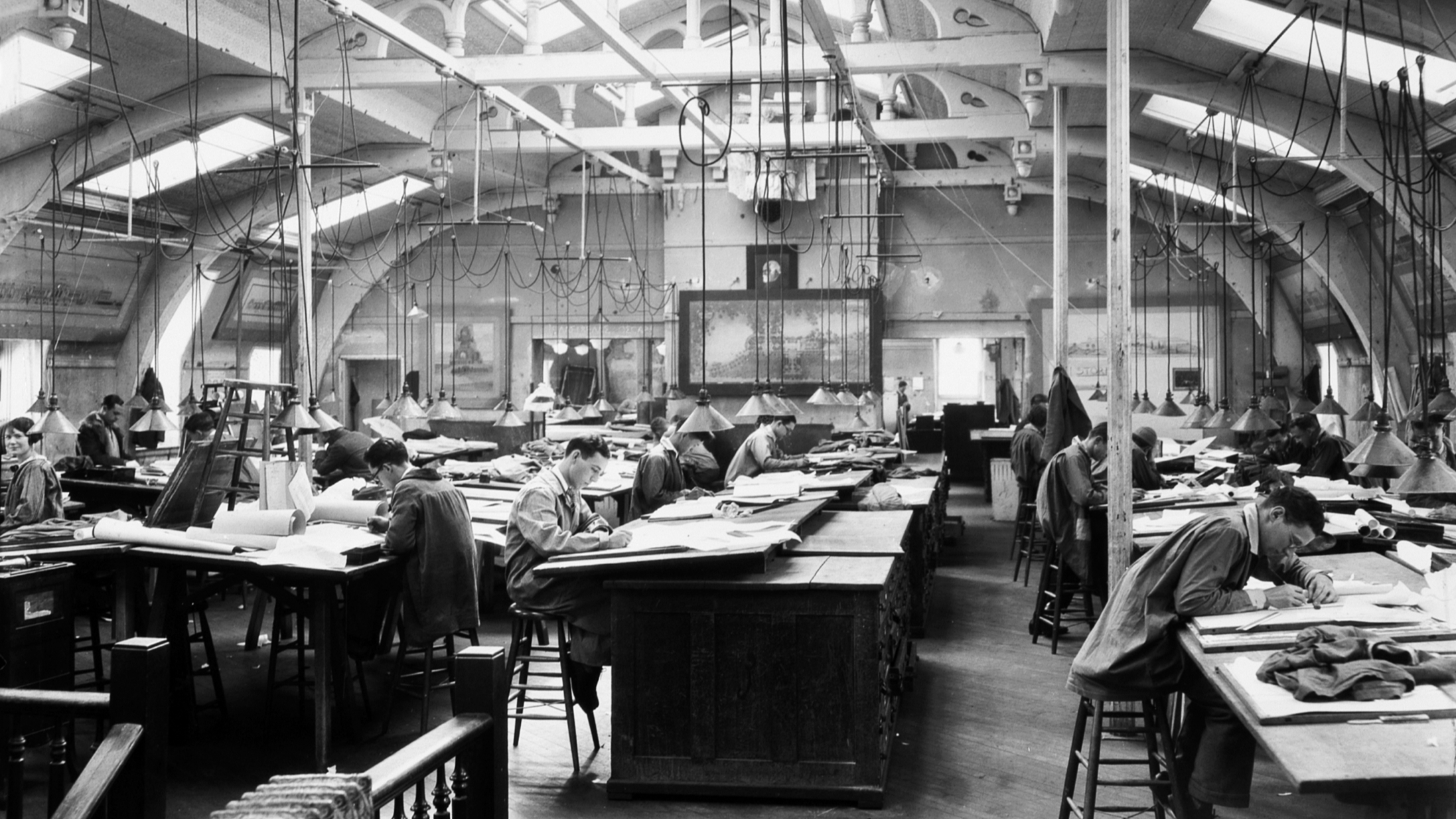 People sitting at desks working with wires and lights hanging from the ceiling.
