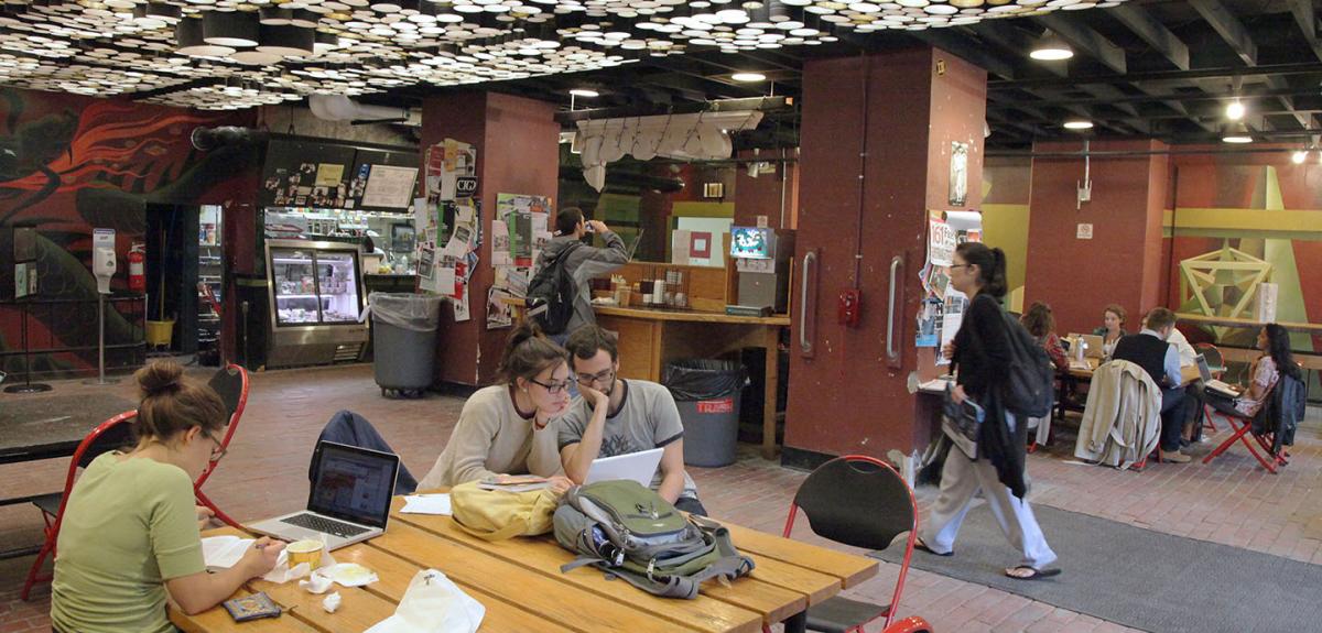 Activity happening in the Green Dragon Cafe including people at tables eating and working on computers.