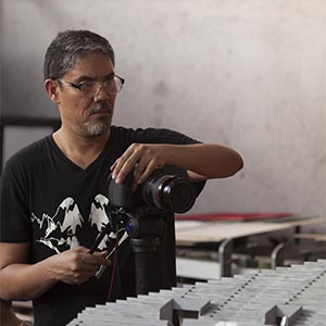 A person wearing glasses holding a camera and taking photos of items on a table.