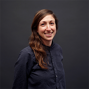 A woman with long brown hair and a black shirt smiles at the camera.