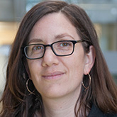 woman with long brown hair and dark rectangle framed glasses. 