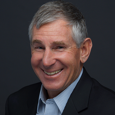 White man with grey hair wearing a blue shirt and dark suit jacket