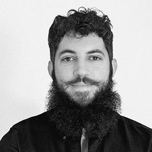 A person with facial hair wearing a dark zippered top