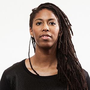 A woman with long brown braids looking at the camera in front of a white background