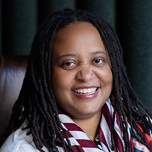 Smiling woman with black hair, a white shirt, and a maroon and white scarf 
