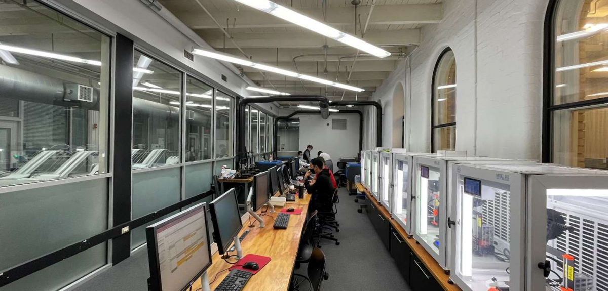 students sitting at desks with 3d printers behind them in a corridor 