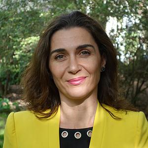 A woman with long brown hair and a yellow blazer smiling at the camera