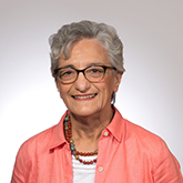 woman with short grey hair wearing a pink shirt with round glasses