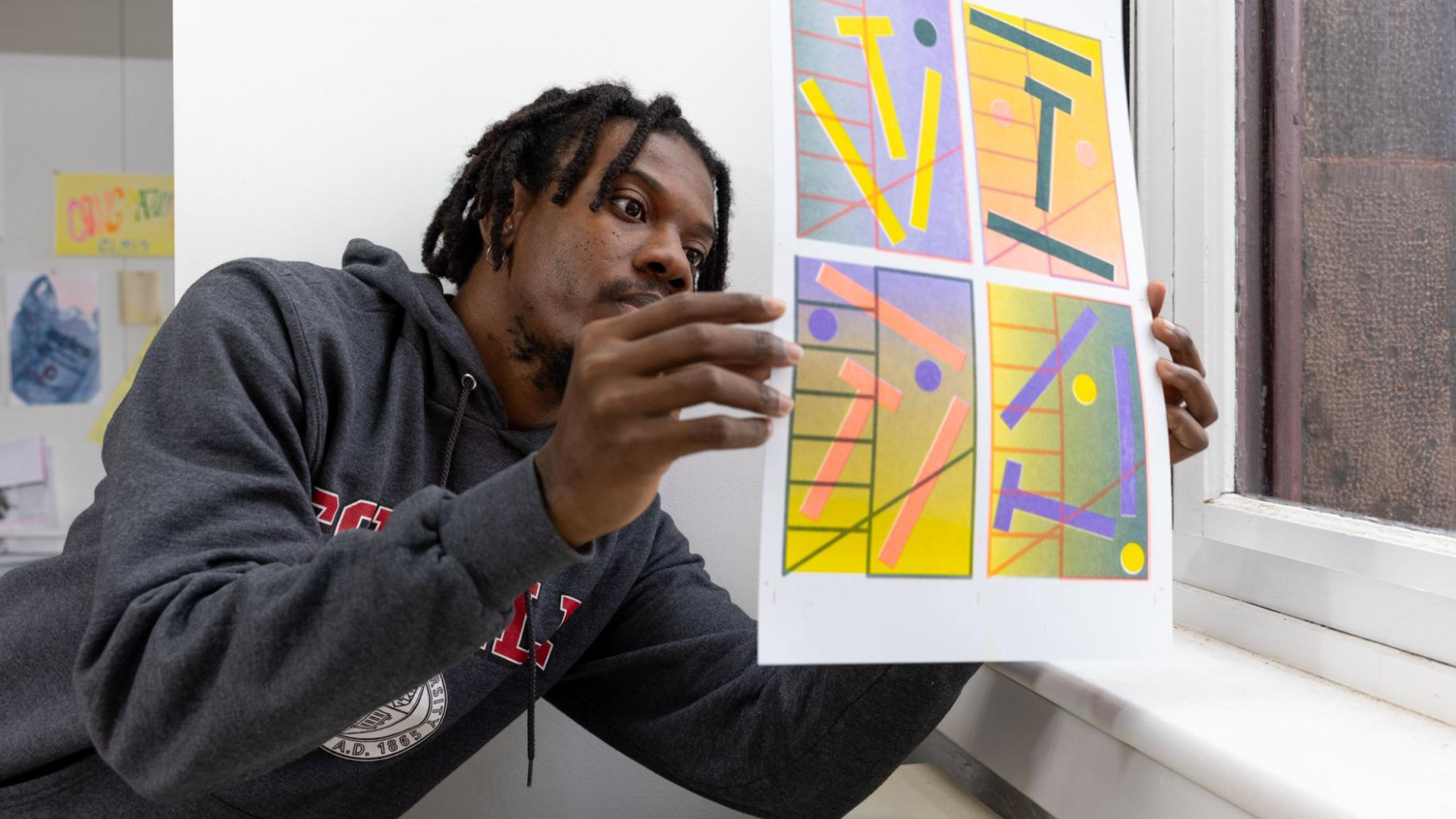 Student examines brightly colored printed poster near a window.