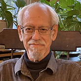 man with a short grey and white beard and glasses and grey collared shirt