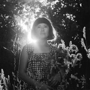 A person holding a bouquet of sunflowers in a forested area with sun shining from behind