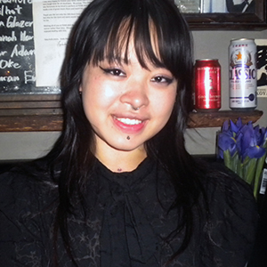 An Asian woman with long, straight, black hair and bangs, wearing winged eyeliner and a black blouse.
