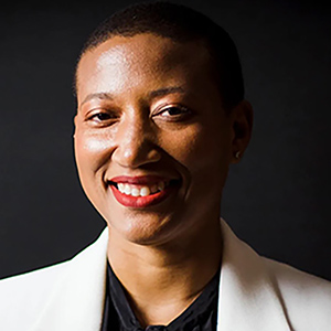 Smiling woman with short black hair, a black top, and a white jacket