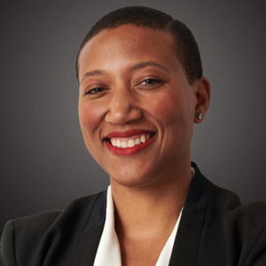 A woman with very short hair looking at the camera smiling in front of a grey background