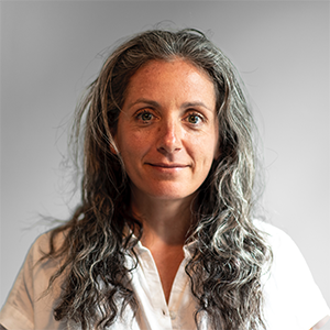 A woman with long hair and a white shirt looks at the camera.
