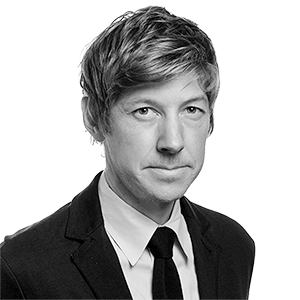 A person with thick light-colored hair, a tie and suit jacket