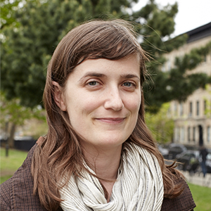 A woman with brown hair wearing a white scarf looks at the camera.
