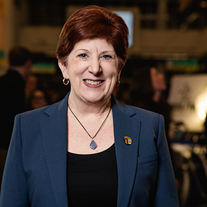 A woman with short hair wearing a dark blue blazer and black shirt smiles at the camera.