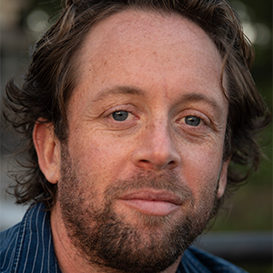 person with blue striped shirt and beard looking at the camera