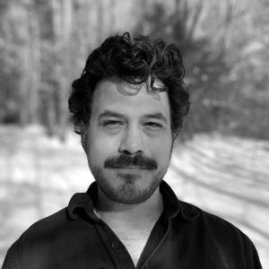 Man with dark hair and mustache in a black shirt in a snowy landscape