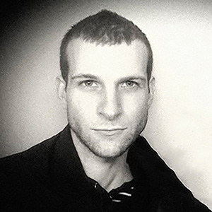 A man with light skin and shortly cropped brown hair, wearing a black shirt.