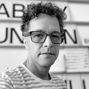 A person with large spectacles, curly hair, and a striped shirt.