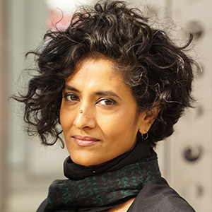 A woman with short black hair and a black scarf looks at the camera.