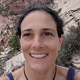 woman with dark hair smiling wearing a dark tank top and black necklace