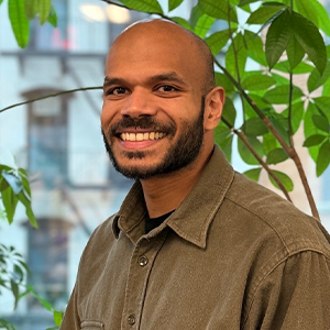 A man with a short beard and wearing an olive green shirt smiles at the camera.