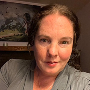 woman wearing a necklace and grey shirt with a framed picture in the backround.