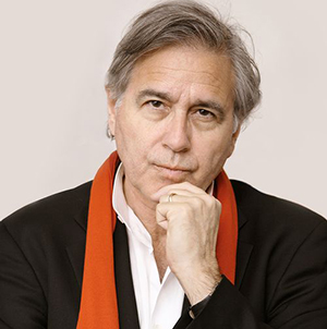 a white man with greyish hair wearing a suit jacket and orange scarf