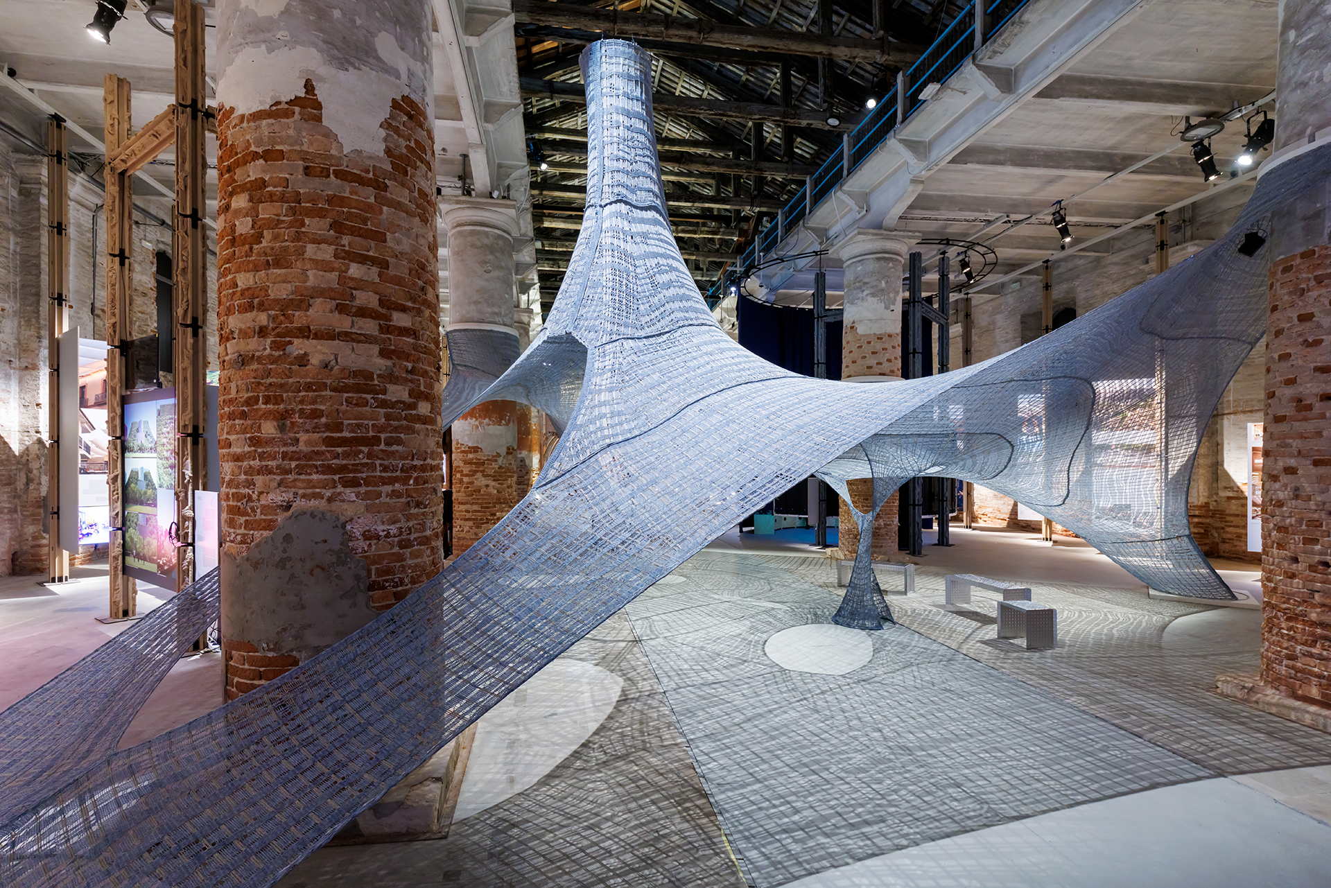 Knitted natural fibers woven to create a structure hanging from the ceiling inside a brick-walled space