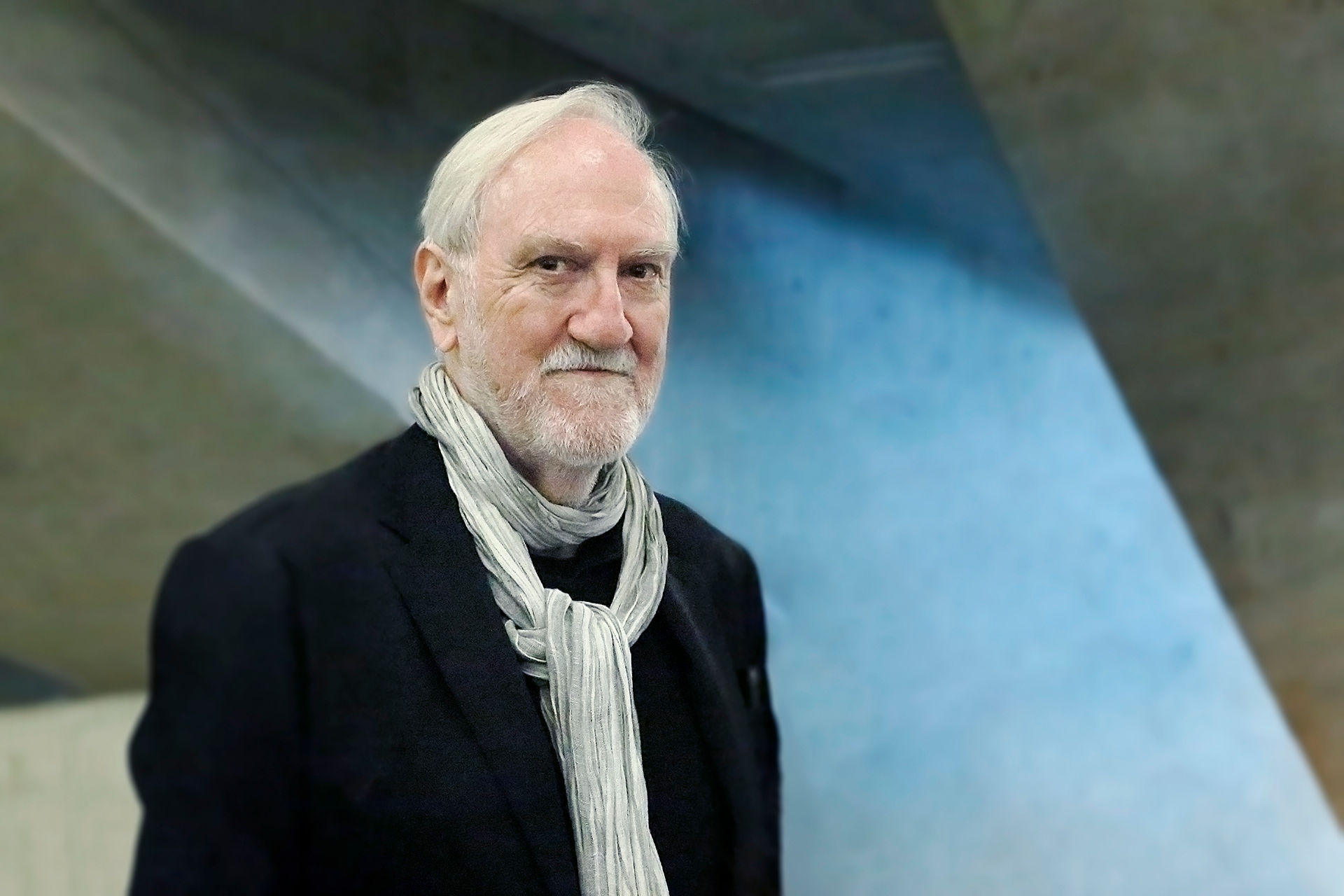 Older man with white hair wearing a black sport coat and white scarf
