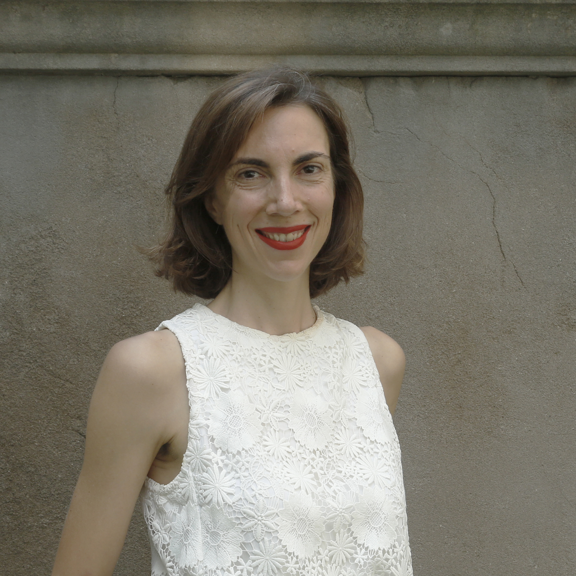 A person with short hair smiling and wearing a white top.