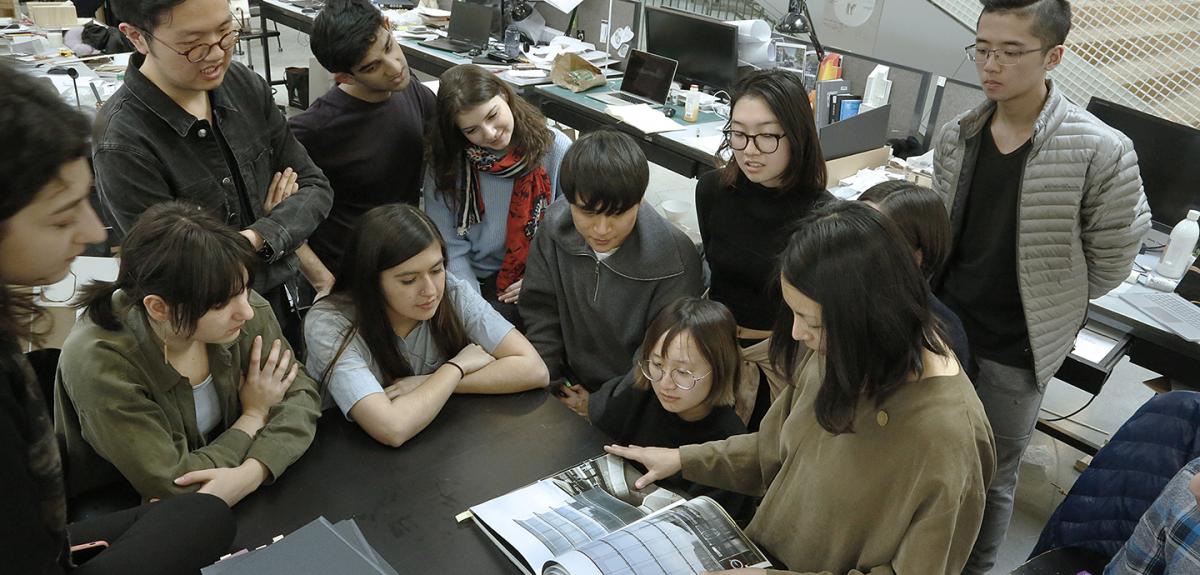 group of students and a faculty member gathered around a book they are discussing