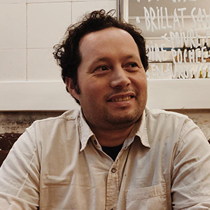 A man with wavy brown hair and a receding hairline, wearing a khaki-colored button-down shirt.