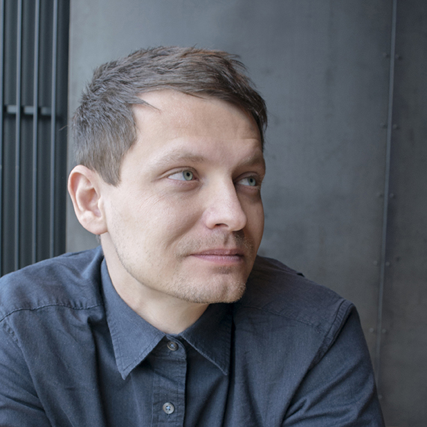 A person with short brown hair wearing a blue button down shirt.