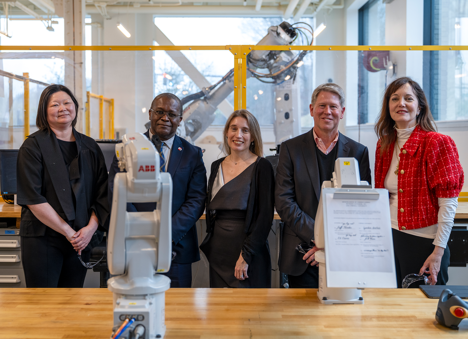 Group of people standing behind a table with two mounted robotic arms and an executed document