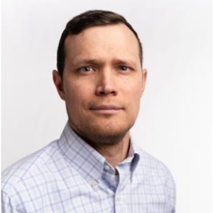A man with short hair and a collared shirt looks at the camera.