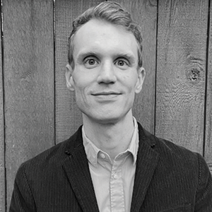 A man with short hair, a dark jacket and light shirt smiles at the camera.