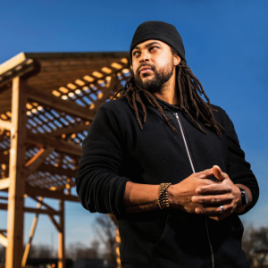 A man posing in front of a wooden frame of a building