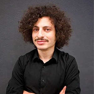 A man with a mustache and a black shirt looks at the camera.