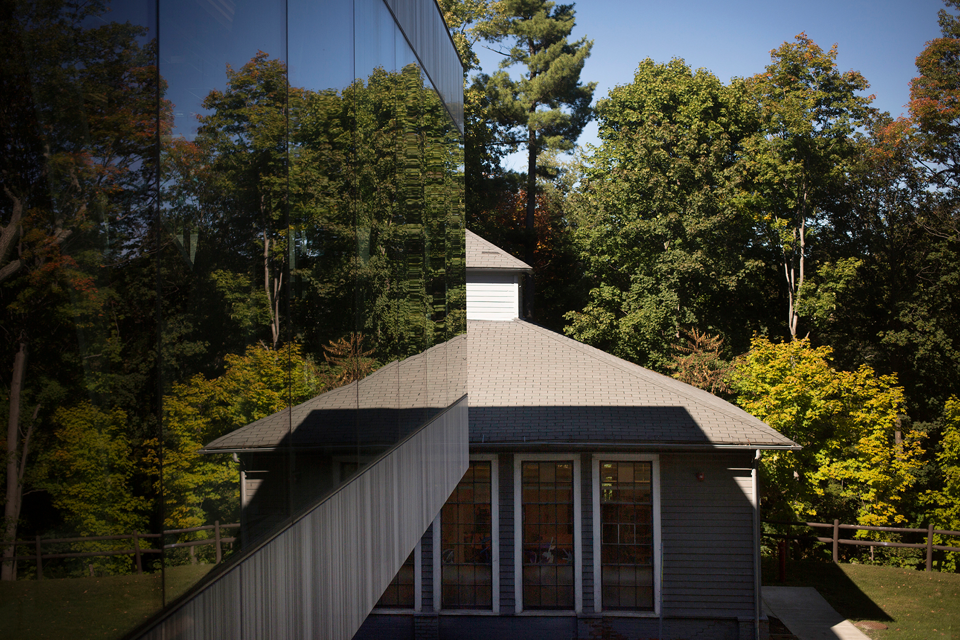 A building façade of windows and another building surrounded by trees and a blue sky in the background.