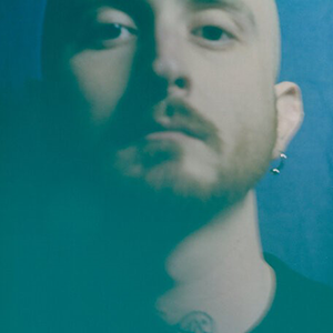 Bald person with light skin and a short red beard looks sternly at the viewer in front of a blue background.