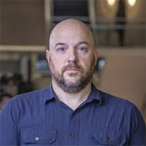 A man with a short beard in a blue shirt looks at the camera.
