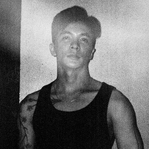 A man with dark hair and a tattoo on his arm, wearing a black tank top.