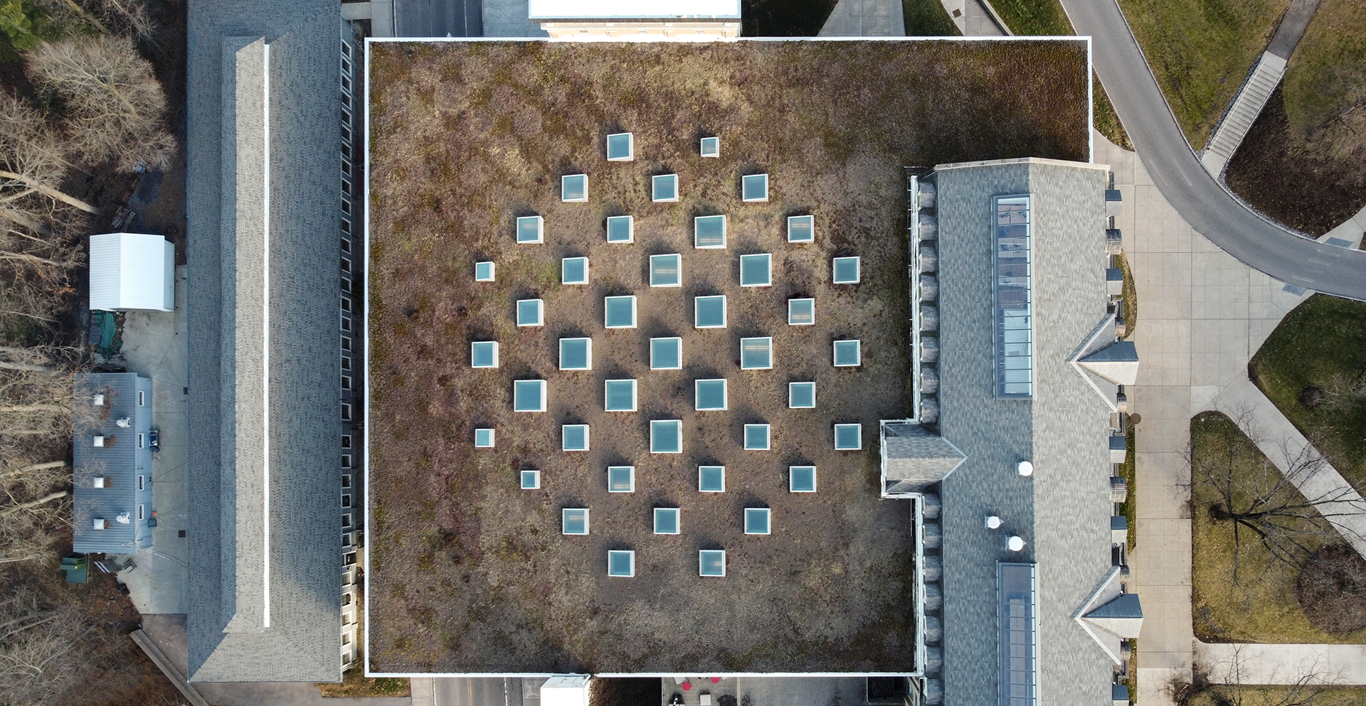 Aerial view of large building rooftops with trees and sidewalks surrounding.
