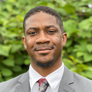 A person slightly smiling, with a beard, wearing a suit coat and tie